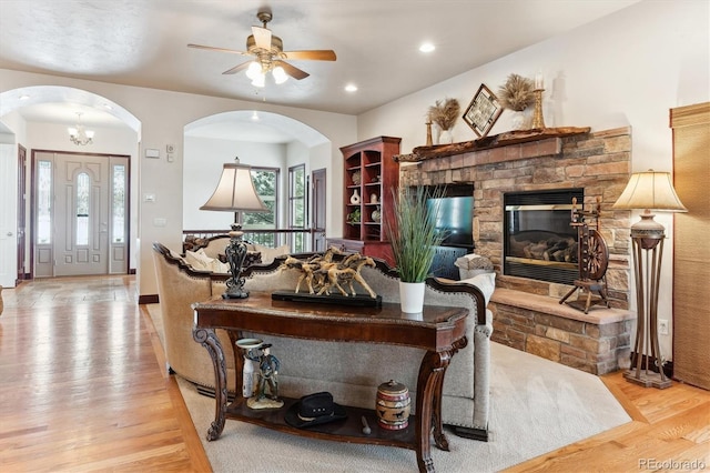 living room featuring ceiling fan, a stone fireplace, and light hardwood / wood-style flooring