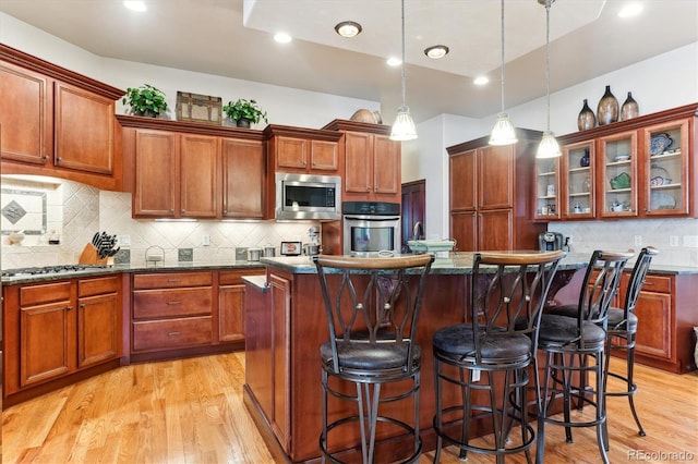 kitchen with stainless steel appliances, a center island, hanging light fixtures, and dark stone counters