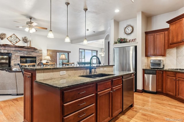 kitchen featuring sink, hanging light fixtures, appliances with stainless steel finishes, an island with sink, and a fireplace