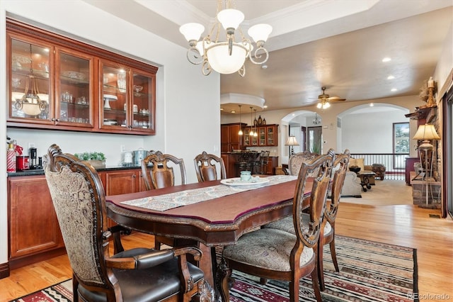 dining room with a raised ceiling, ceiling fan with notable chandelier, and light wood-type flooring