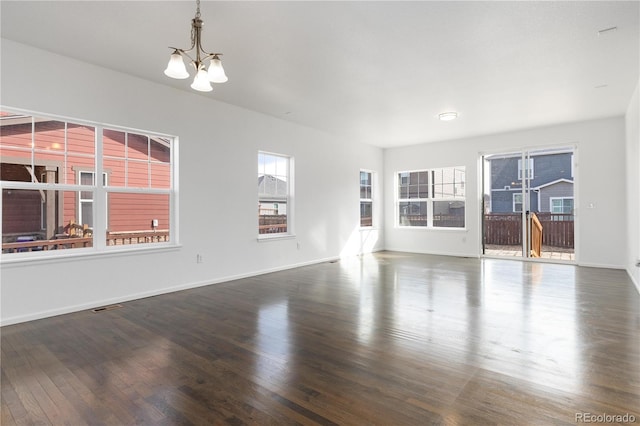 empty room with baseboards, visible vents, a chandelier, and wood finished floors