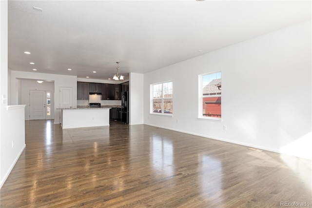 unfurnished living room with recessed lighting, dark wood finished floors, baseboards, and an inviting chandelier