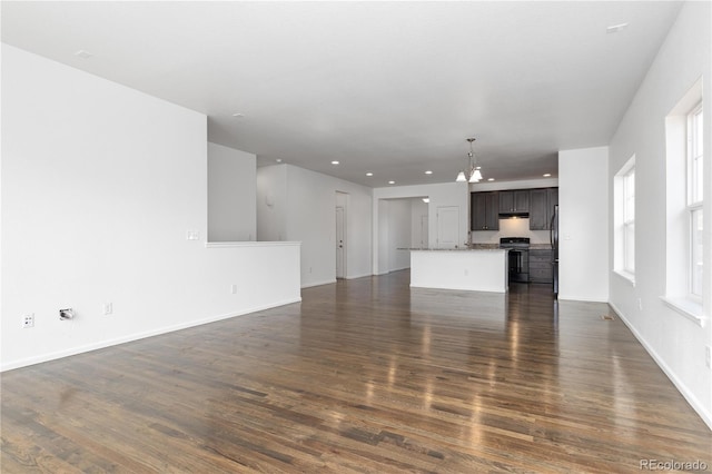 unfurnished living room with recessed lighting, dark wood-style flooring, a notable chandelier, and baseboards