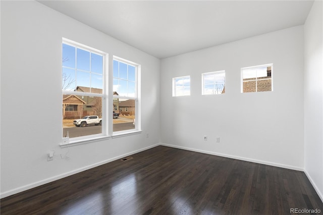 spare room with dark wood-style flooring, visible vents, and baseboards