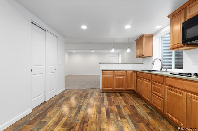 kitchen featuring light countertops, dark wood-type flooring, a sink, a peninsula, and black appliances