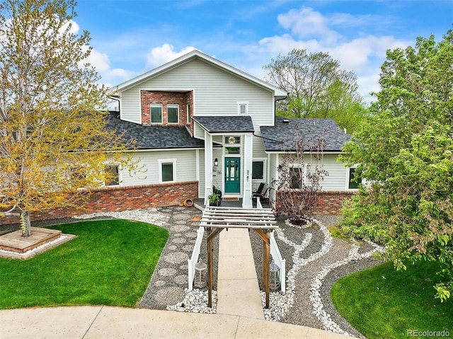 view of front of home with brick siding, a front yard, and roof with shingles