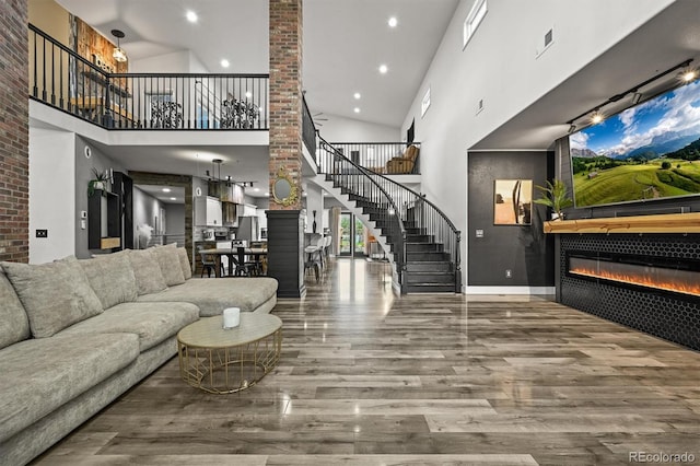 living area with stairs, a towering ceiling, wood finished floors, a glass covered fireplace, and baseboards