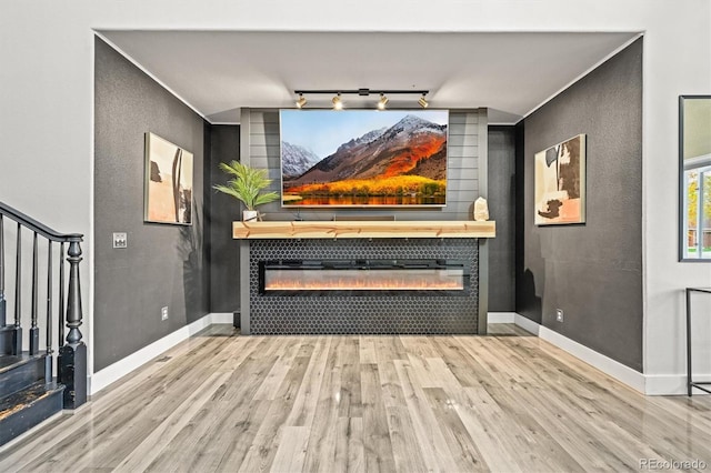 unfurnished living room featuring a tiled fireplace, wood finished floors, baseboards, and stairs