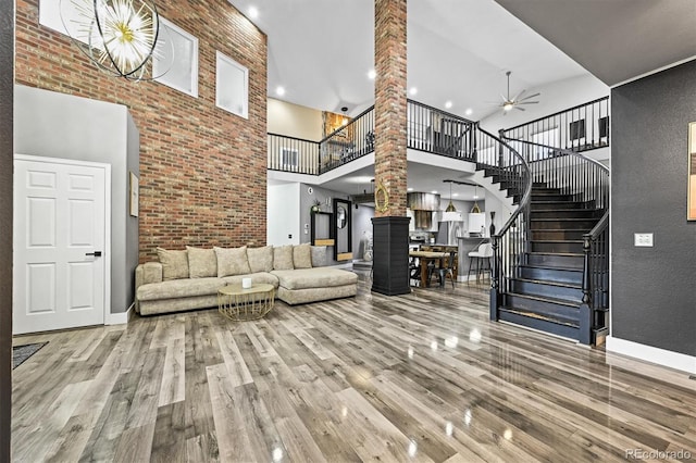 living room featuring ornate columns, a high ceiling, wood finished floors, stairway, and ceiling fan