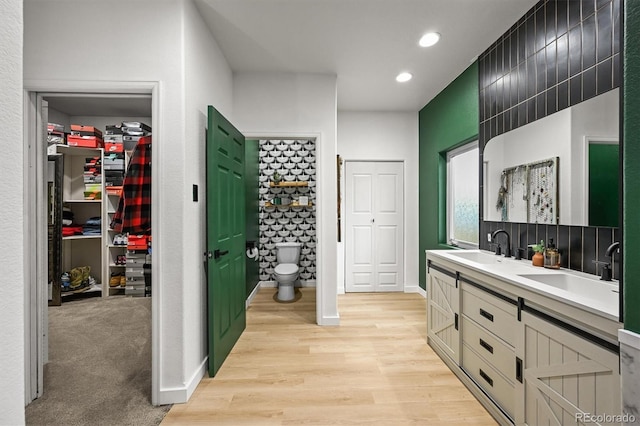 full bathroom featuring toilet, double vanity, wood finished floors, recessed lighting, and a spacious closet