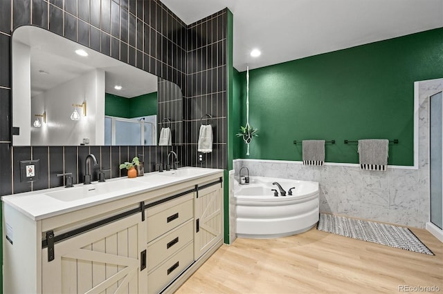 full bathroom with tile walls, wood finished floors, a garden tub, a stall shower, and double vanity