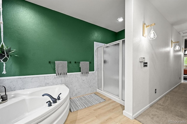 full bath with a shower stall, a bath, wood finished floors, a textured wall, and a wainscoted wall