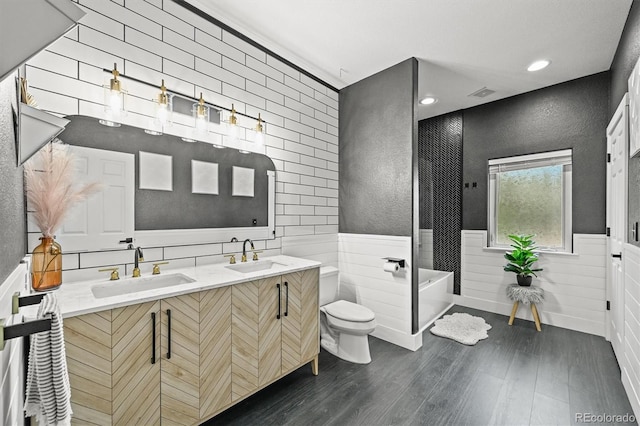 bathroom featuring wainscoting, a soaking tub, wood finished floors, double vanity, and toilet