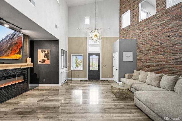 foyer featuring a towering ceiling, wood finished floors, a glass covered fireplace, baseboards, and brick wall