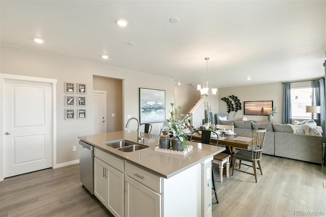 kitchen with sink, hanging light fixtures, a center island with sink, stainless steel dishwasher, and white cabinets