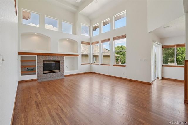 2247 Eagles Nest Dr, Lafayette, CO 80026 - unfurnished living room with wood finished floors, a tiled fireplace, a towering ceiling, and built in features