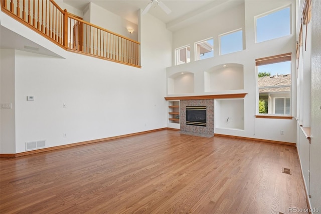 2247 Eagles Nest Dr, Lafayette, CO 80026 - unfurnished living room featuring wood finished floors, a tiled fireplace, a towering ceiling, ceiling fan, and built in features