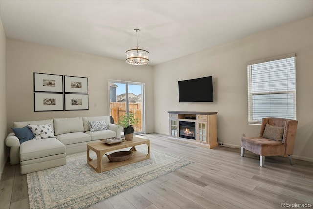 living room with a chandelier, a glass covered fireplace, light wood-style flooring, and baseboards