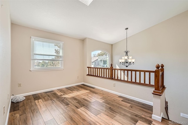 unfurnished room featuring a notable chandelier, plenty of natural light, and hardwood / wood-style floors