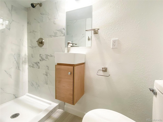 bathroom with a tile shower, vanity, and toilet