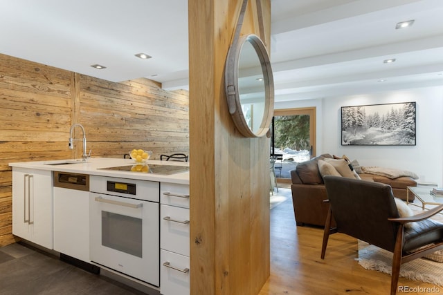 kitchen featuring dark wood-type flooring, oven, sink, wooden walls, and cooktop