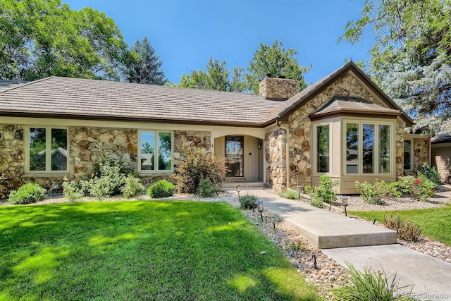 view of front of property featuring stone siding, a front lawn, and a chimney