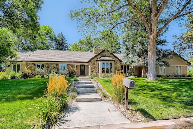 single story home with a front yard, stone siding, a tile roof, and a chimney