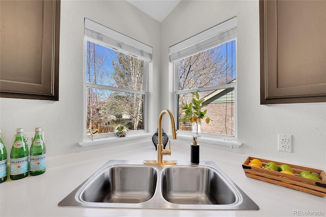 interior details with dark brown cabinets, light countertops, a textured wall, and a sink