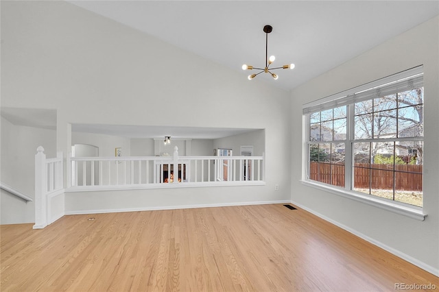 empty room featuring a chandelier, baseboards, light wood-type flooring, and lofted ceiling