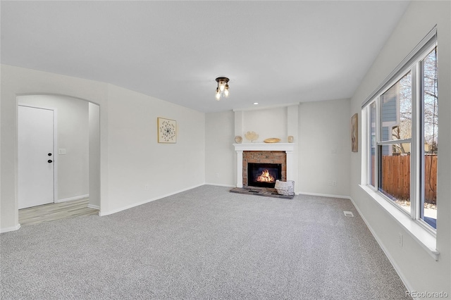 unfurnished living room featuring baseboards, plenty of natural light, carpet, and a brick fireplace