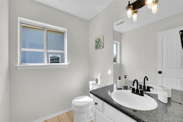 bathroom featuring vanity, wood finished floors, baseboards, visible vents, and toilet