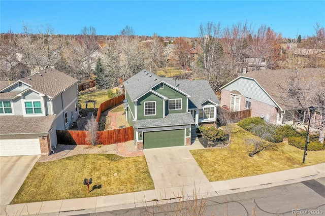 traditional home featuring a front lawn, driveway, fence, a shingled roof, and a garage