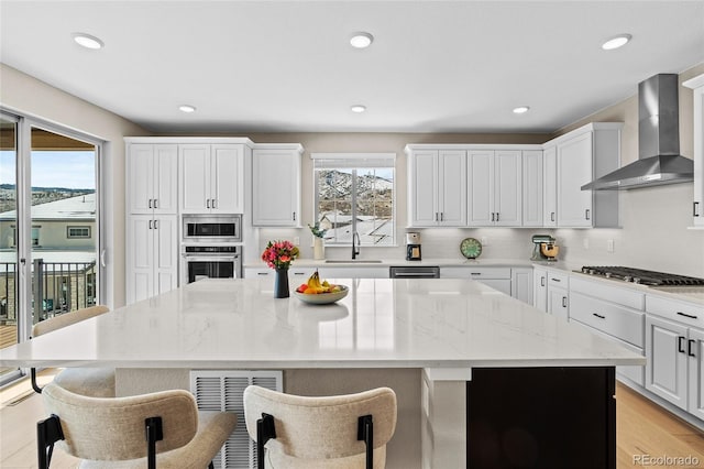 kitchen with light stone countertops, a center island, wall chimney exhaust hood, and appliances with stainless steel finishes