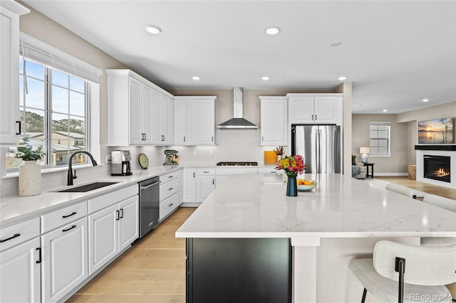 kitchen featuring white cabinets, appliances with stainless steel finishes, sink, and wall chimney range hood