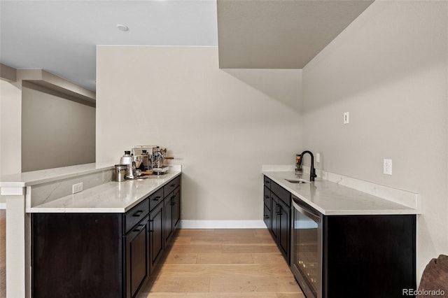 kitchen with sink, wine cooler, light hardwood / wood-style flooring, light stone counters, and kitchen peninsula