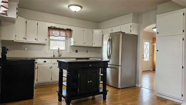 315 W 5th St, Julesburg, CO 80737 - kitchen with white cabinets, arched walkways, a sink, freestanding refrigerator, and black range with electric stovetop