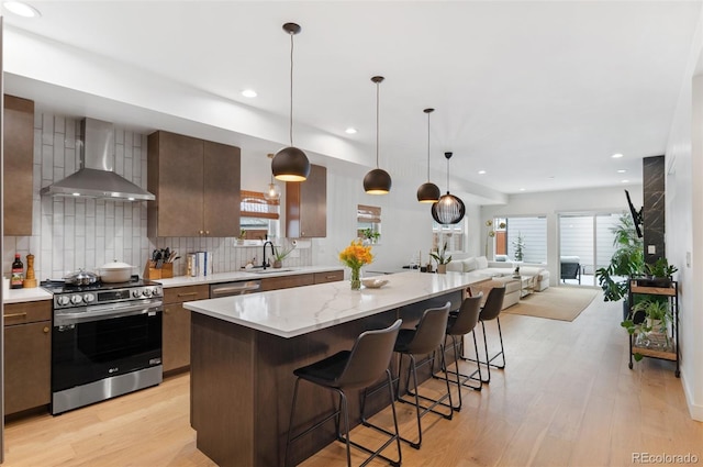 kitchen with decorative backsplash, appliances with stainless steel finishes, sink, wall chimney range hood, and a kitchen island