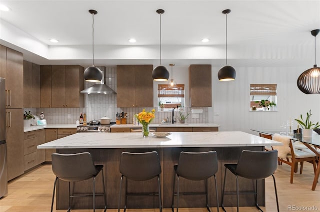 kitchen featuring a large island, decorative light fixtures, wall chimney range hood, and sink