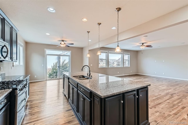 kitchen featuring stainless steel appliances, sink, an island with sink, light stone countertops, and pendant lighting