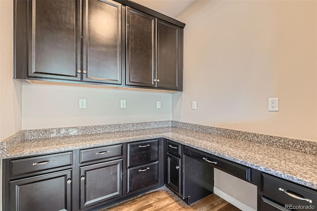 kitchen featuring light stone countertops, light wood-type flooring, and dark brown cabinetry