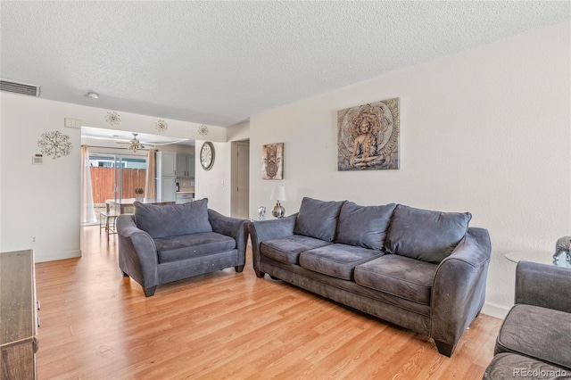 living area featuring a textured ceiling, light wood finished floors, visible vents, and a ceiling fan