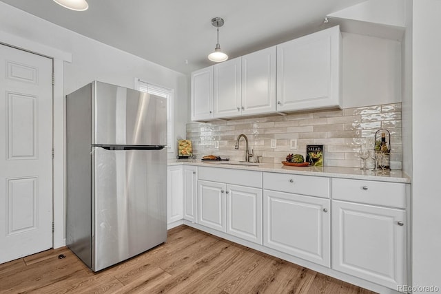 kitchen featuring decorative backsplash, decorative light fixtures, stainless steel refrigerator, white cabinets, and sink