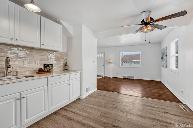 kitchen with light wood-type flooring, sink, decorative backsplash, and white cabinetry