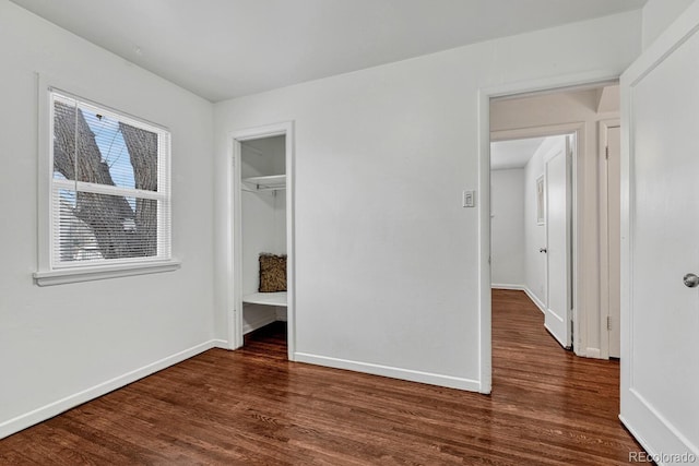 unfurnished bedroom featuring a spacious closet, a closet, and dark wood-type flooring