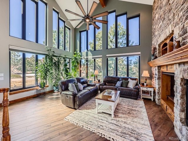 living area with baseboards, a ceiling fan, hardwood / wood-style floors, vaulted ceiling, and a stone fireplace