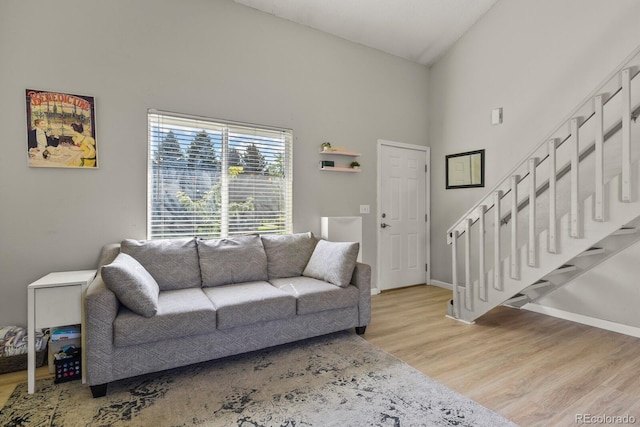 living room with light wood-style flooring, high vaulted ceiling, stairs, and baseboards