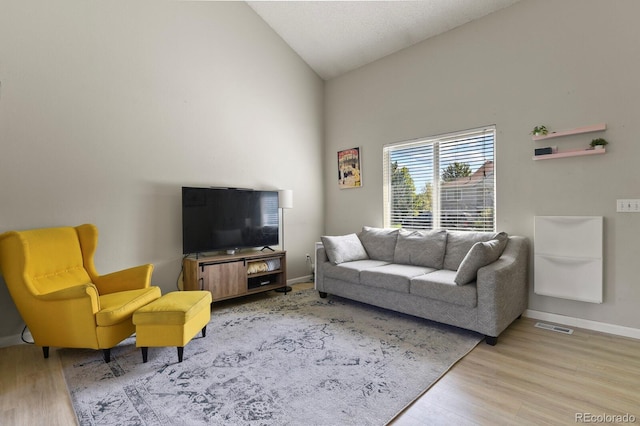 living room featuring visible vents, baseboards, light wood-style floors, and high vaulted ceiling