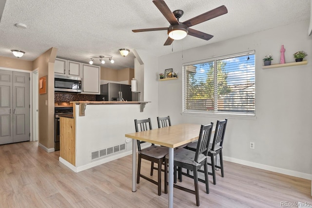 dining area with a textured ceiling, light wood-type flooring, visible vents, and ceiling fan