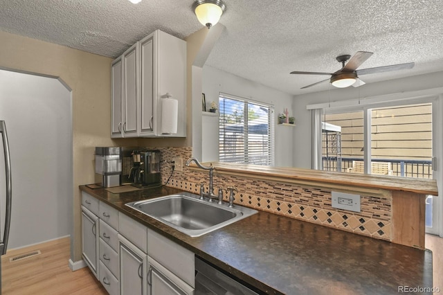 kitchen featuring dark countertops, backsplash, light wood-style floors, a ceiling fan, and a sink