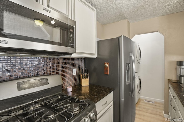 kitchen with visible vents, tasteful backsplash, stacked washing maching and dryer, stainless steel appliances, and white cabinets